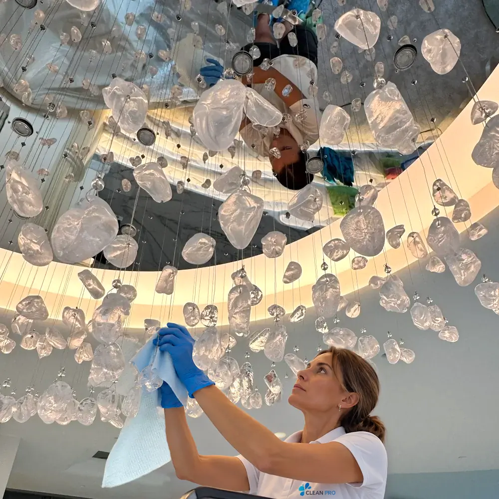 Technicienne Clean Pro nettoyant à la main les pampilles d'un lustre en hauteur